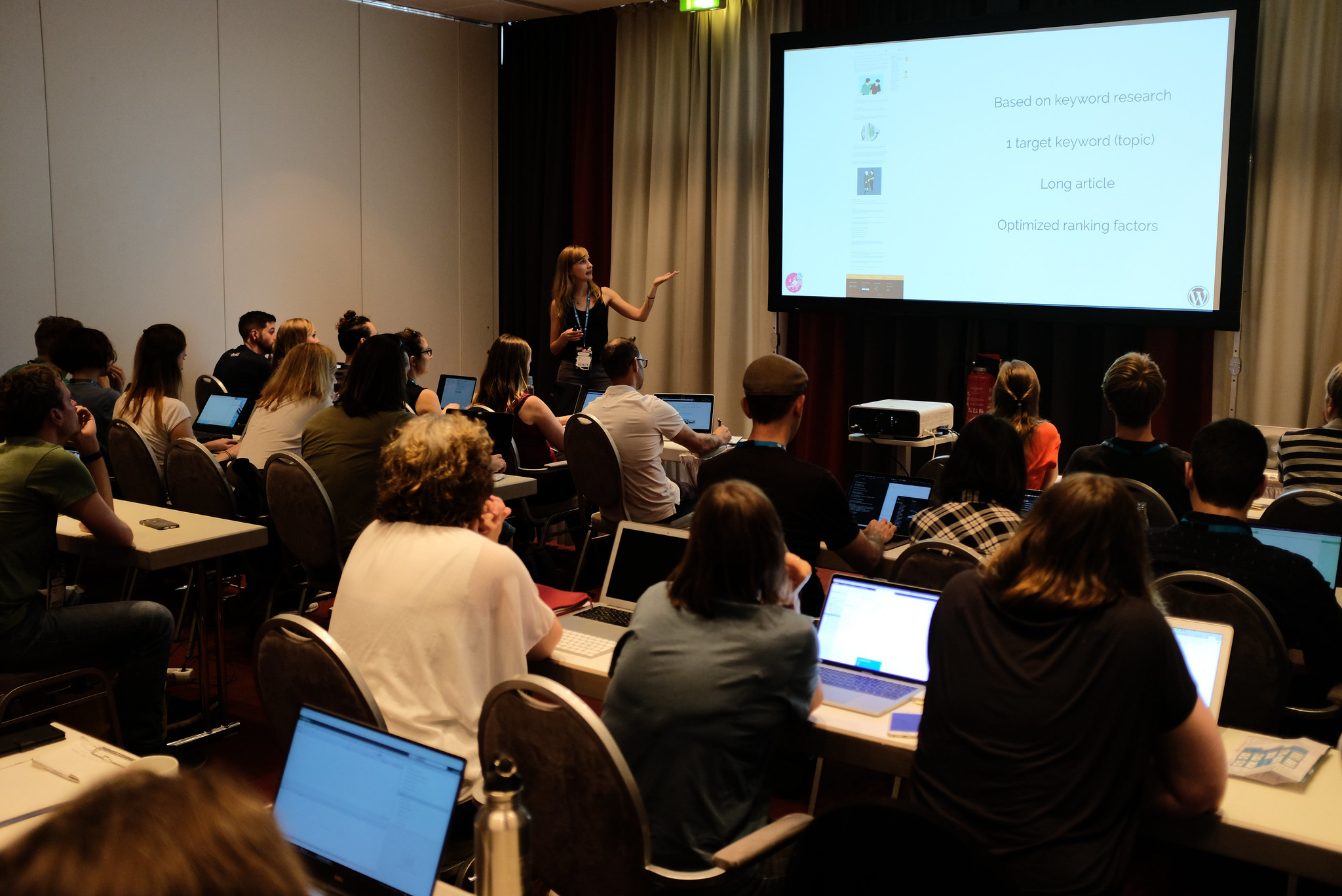 Photo of workshop with attendees watching the host pointing to a computer screen