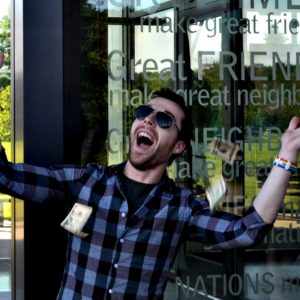 Photo of Matt, wearing sunglasses, smiling outside in front of a glass building.