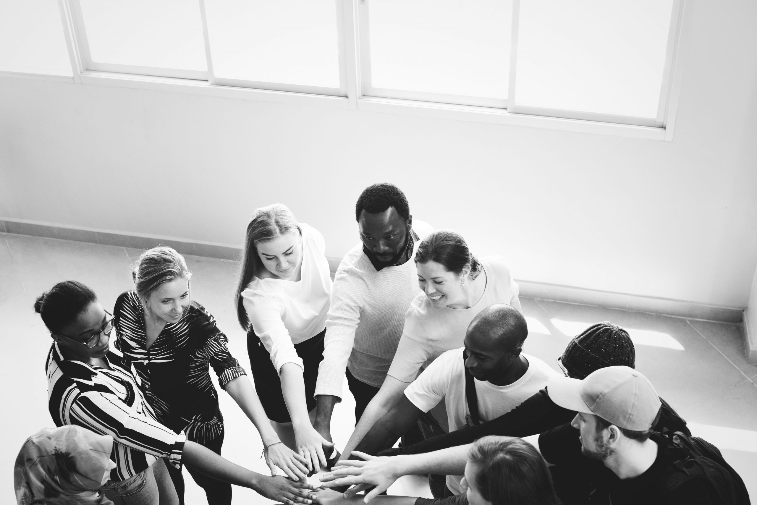 A black and white image of a group of people - black white male and female - putting their hands in as a team