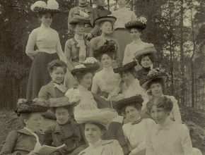 Svartvitt fotografi av en grupp kvinnor i vackra kläder och stora hattar.