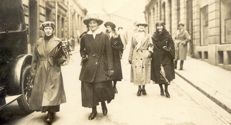Svartvitt foto av fem gående kvinnor på en gata i en stad.