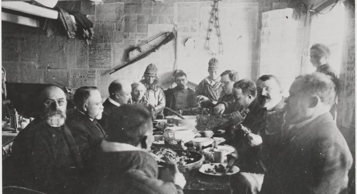 Svartvitt fotografi av ett tjugotal människor som sitter runt ett bord och äter.