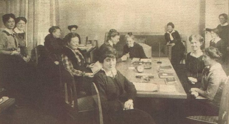 Ett svartvitt fotografi av en grupp kvinnor i ett rum som sitter vid ett bord.