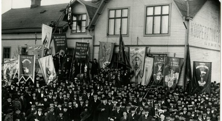 Ett svartvitt fotografi av en folkmassa av män med många fanor och banderoller.