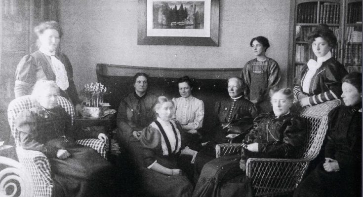 Svartvitt foto av tio kvinnor i ett vardagsrum.