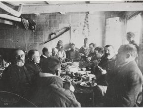 Svartvitt fotografi av ett tjugotal människor som sitter runt ett bord och äter.