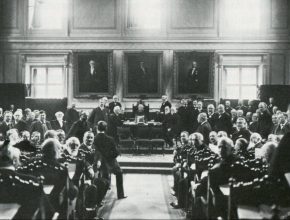 Ett svartvitt fotografi av många män i en sal som vänder sig om och tittar mot kameran.