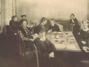 Ett svartvitt fotografi av en grupp kvinnor i ett rum som sitter vid ett bord.