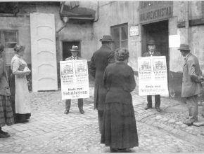 Svartvitt foto av två personer som håller i valaffischer och en grupp människor som tittar på.